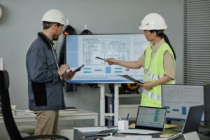 Side view portrait of two engineers reviewing blueprints indoors and pointing at computer screen, copy space